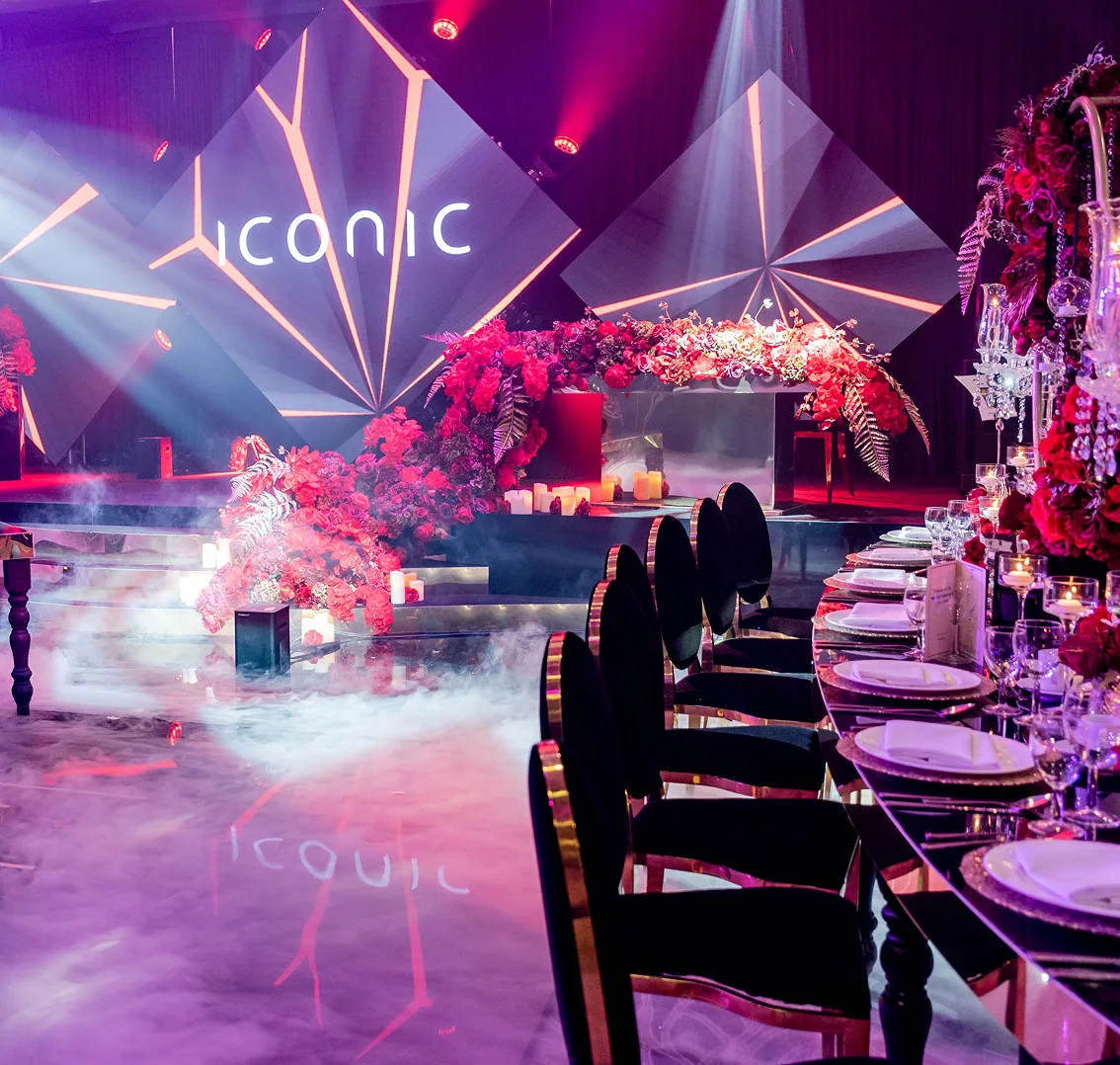 Luxurious event setup with elegant dining, floral decor, and ambient lighting under iconic signage on stage.