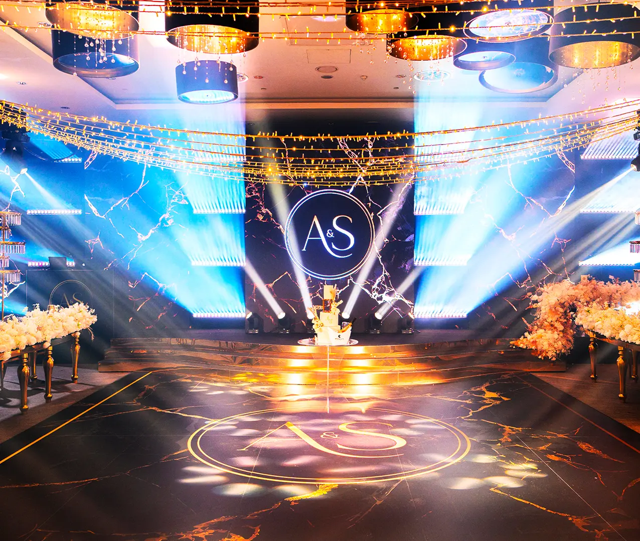 Luxurious wedding stage with illuminated A & S design, elegant florals, and sophisticated lighting effects.