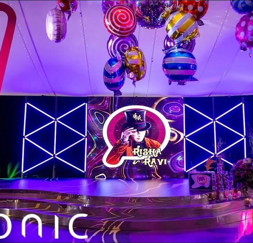 Vibrant party stage with colorful balloons and neon lights showcasing a themed digital display for Risha and Ravi.