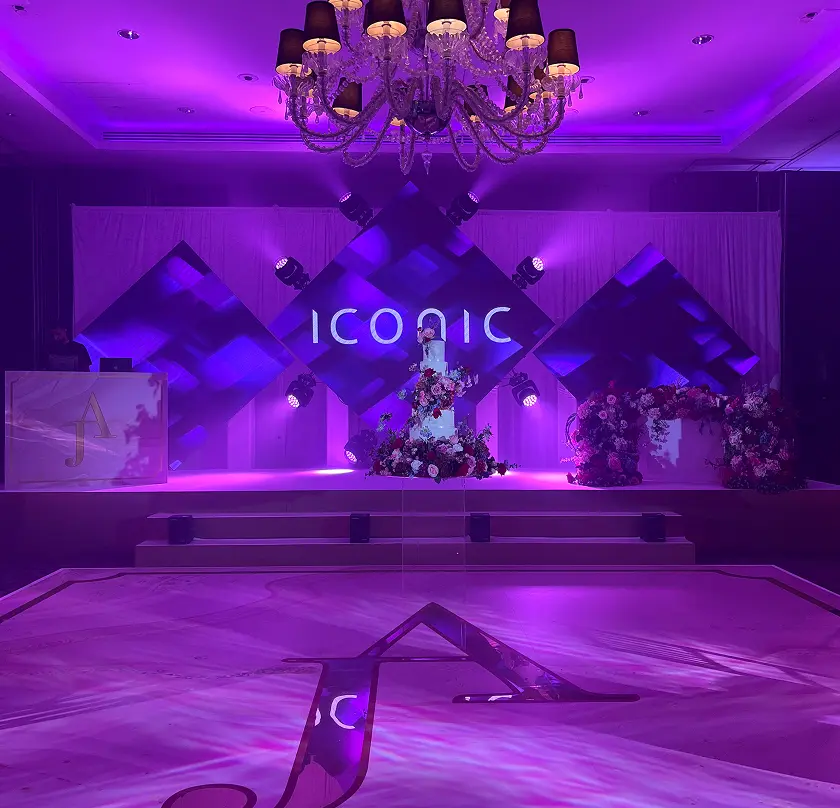 Lavish purple-lit stage with floral decorations under a grand chandelier, Iconic text illuminated at the venue.
