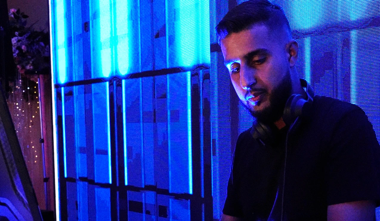 DJ performing live with blue lights and headphones, creating an energetic atmosphere at a club event.