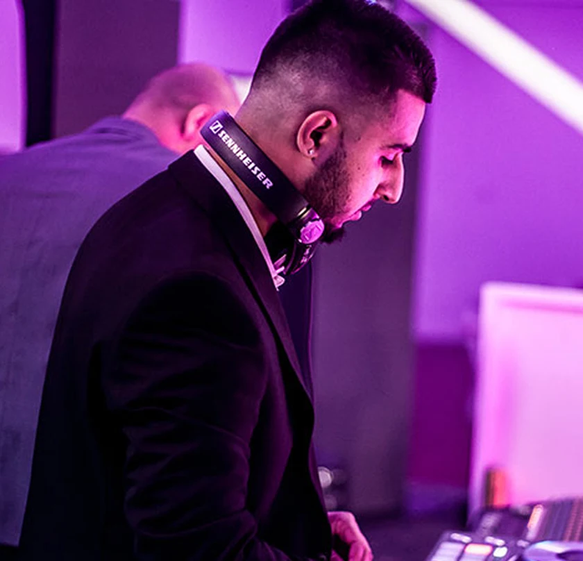 DJ focused on mixing music at an event, wearing headphones with purple lighting ambiance.