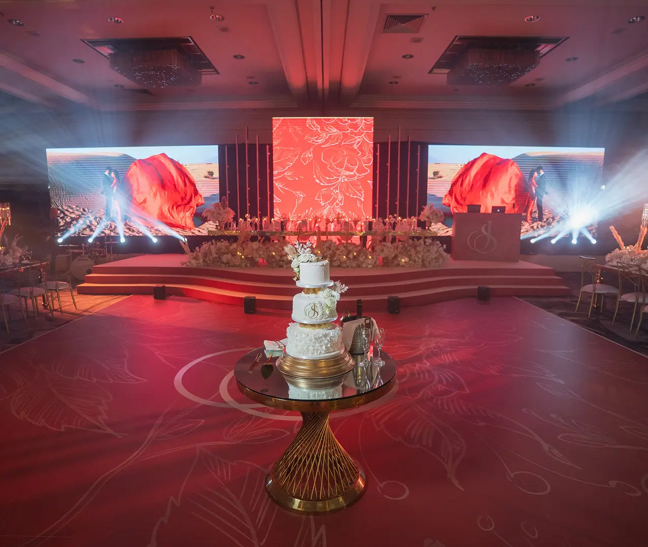 Luxurious wedding venue with ornate cake, floral decor, and vibrant LED screens creating an elegant ambiance.